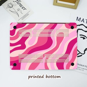 May include: A pink and light pink patterned laptop case with a wavy design. The case has a printed bottom and black corner accents. The case has ventilation slots for cooling.