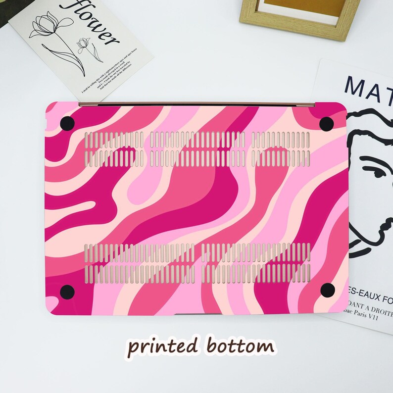 May include: A pink and light pink patterned laptop case with a wavy design. The case has a printed bottom and black corner accents. The case has ventilation slots for cooling.