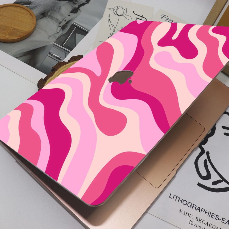 May include: A laptop with a pink and white wavy pattern cover. The design features shades of pink, creating a vibrant and eye-catching aesthetic. The laptop is open, revealing the keyboard and trackpad.