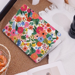 May include: A laptop case with a vibrant floral pattern featuring pink, orange, blue, and yellow flowers on a white background. The case has a cutout for the Apple logo. The design includes green leaves and stems, creating a colorful and cheerful aesthetic.