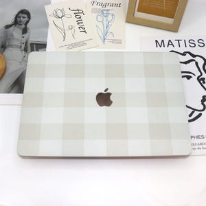 Può includere: Un computer portatile bianco con un motivo a scacchi beige e bianco. Il logo Apple è visibile sul davanti del laptop.