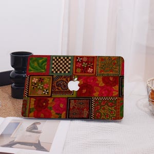 May include: A laptop case with a patchwork design featuring floral, paisley, and checkered patterns in red, green, and gold. The Apple logo is visible in the centre. The case is on a white surface.
