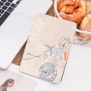 Peut inclure: Une housse de tablette beige sur le thème du voyage, avec un avion stylisé et le texte "where next...?" ainsi que divers tampons de voyage. Les tampons incluent "Paris, France" et "Berlin C2".