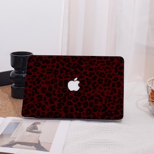 May include: A laptop case featuring a burgundy leopard print design. The case has a white Apple logo in the center. The case is on a white surface.