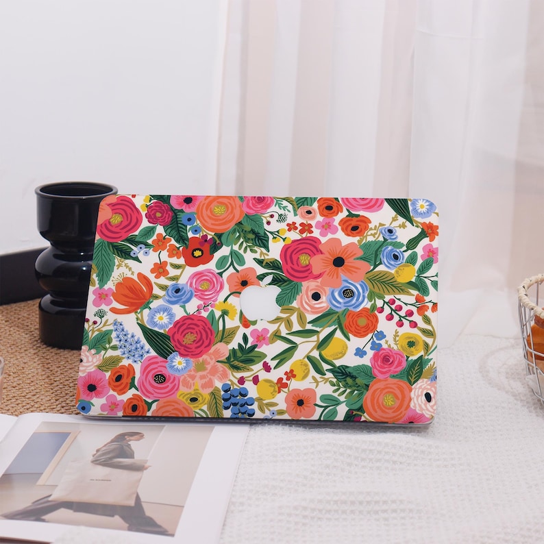 May include: A laptop case with a vibrant floral pattern. The design features a white background covered in colorful flowers, including pink, orange, and blue blooms, with green leaves. The case has a cutout for the Apple logo.