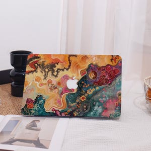 Op de afbeelding: Een laptophoesje met een levendig, abstract ontwerp en een wit Apple-logo. De hoes toont een kleurrijke mix van oranje, gele, groene en roze tinten, waardoor een unieke en artistieke esthetiek ontstaat. Het ontwerp lijkt op een aquarel.