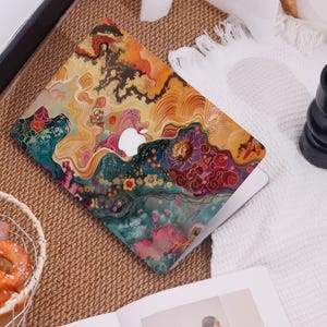Op de afbeelding: Een laptop met een kleurrijk, abstract ontwerp. De hoes heeft een levendige mix van oranje, geel, blauwgroen en roze tinten, met een zichtbaar wit Apple-logo. Het ontwerp lijkt op een aquarel met bloemen- en vloeiende patronen.