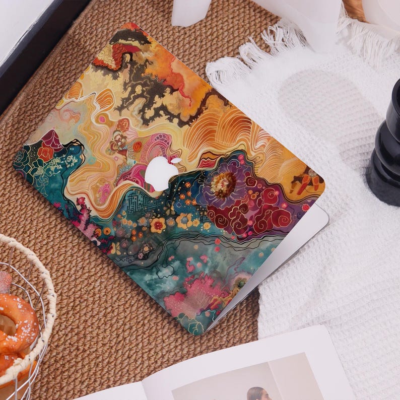 Op de afbeelding: Een laptop met een kleurrijk, abstract ontwerp. De hoes heeft een levendige mix van oranje, geel, blauwgroen en roze tinten, met een zichtbaar wit Apple-logo. Het ontwerp lijkt op een aquarel met bloemen- en vloeiende patronen.