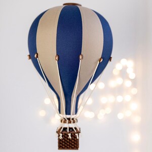 May include: A decorative hot air balloon with a blue and tan striped pattern. The balloon has a brown wooden basket and accents. White cords connect the basket to the balloon. The balloon is a decorative item.