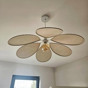 May include: Ceiling fan with five beige, petal-shaped blades. The fan has a central light fixture with a vintage-style bulb. The fixture is mounted on a white ceiling. The text "fly with us" is in the upper right corner.