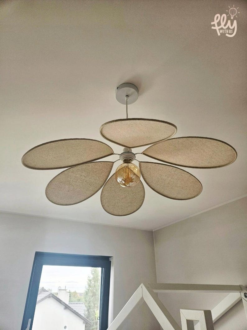 May include: Ceiling fan with five beige, petal-shaped blades. The fan has a central light fixture with a vintage-style bulb. The fixture is mounted on a white ceiling. The text "fly with us" is in the upper right corner.
