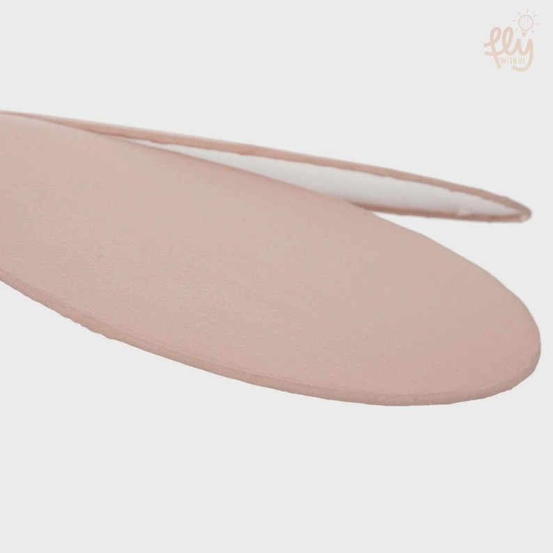 May include: Close-up of a light pink, oval-shaped object with a white interior. The object has a smooth, matte finish and appears to be made of wood or a similar material. The background is a plain, light gray.