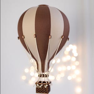 May include: A brown and white striped hot air balloon with a wicker basket hanging below. The balloon is suspended from the ceiling with a string.