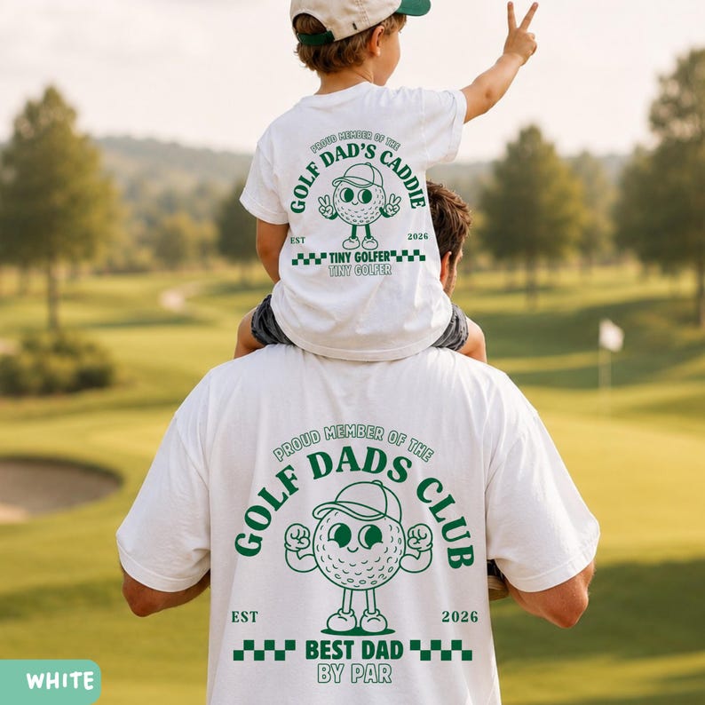 May include: White t-shirts with green text and graphics. The shirts feature a golf ball character with a cap and the phrases "Golf Dad's Caddie" and "Golf Dads Club". The text "Best Dad By Par" is also visible. A child is sitting on a person's shoulders.