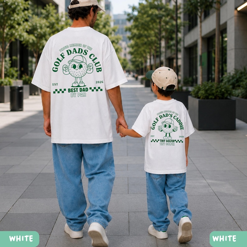 May include: Two white t-shirts with green text and graphics. One shirt reads "GOLF DADS CLUB" with a golf ball graphic and "BEST DAD BY PAR." The other says "GOLF DAD'S CADDIE" with a golf ball graphic and "TINY GOLFER."