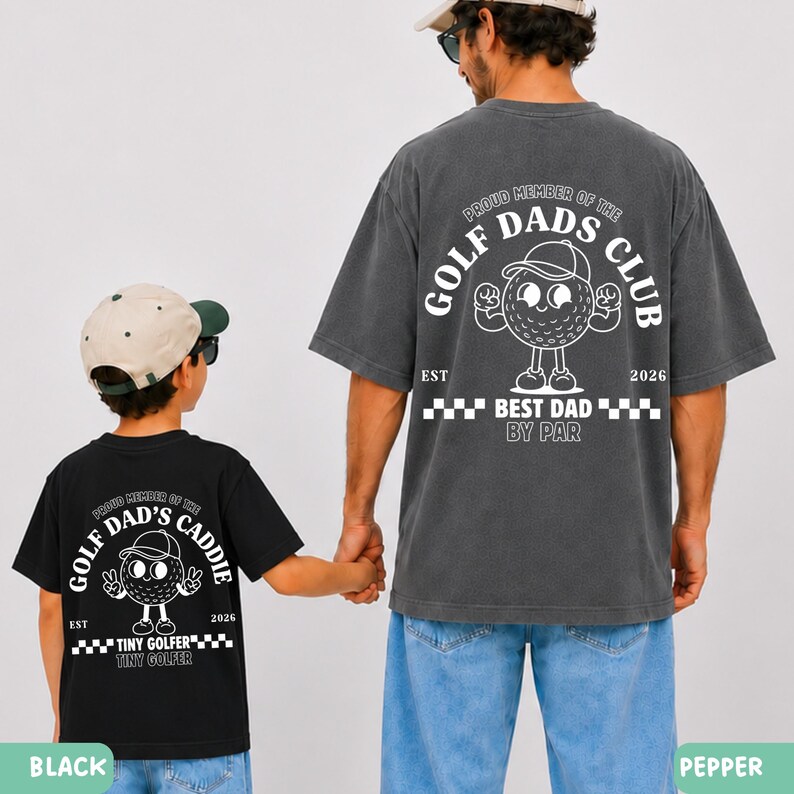 May include: Two matching t-shirts, one black and one pepper-colored, featuring a golf ball character with the text "Golf Dad's Club" and "Best Dad By Par." The black shirt says "Tiny Golfer". The shirts are worn by a father and child.