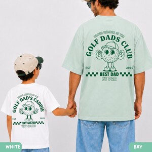 May include: A white t-shirt with a golf-themed graphic that reads "Proud Member of the Golf Dad's Caddie" and "Tiny Golfer". A light green t-shirt with a golf-themed graphic that reads "Proud Member of the Golf Dad's Club" and "Best Dad By Par".