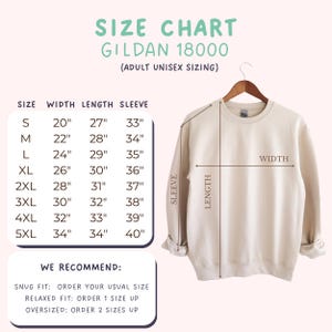Op de afbeelding: Een beige Gildan 18000 unisex sweatshirt voor volwassenen hangt aan een houten hanger. Een maattabel toont de afmetingen in inches voor breedte, lengte en mouwlengte, vari&euml;rend van maat S tot 5XL. De tabel bevat aanbevelingen voor de pasvorm.
