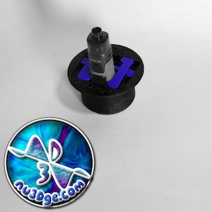 May include: A black 3D printed stand with a blue plastic insert to hold a black and silver vape. The stand has the word "AU3DGE.COM" printed on it.