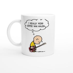 May include: White ceramic mug with a cartoon character playing a guitar. The character is thinking about Eddie Van Halen. The text on the mug reads "I really miss Eddie Van Halen".