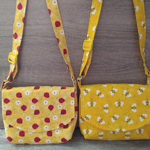 May include: Two yellow fabric purses with adjustable straps. One purse has a ladybug print and the other has a bee print.