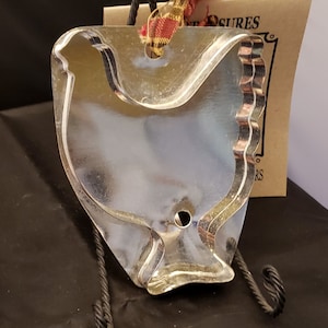May include: A silver metal cookie cutter shaped like a chicken. The cutter has a hole at the top for hanging. The cutter is on a black stand. The text "One Treasures" is visible on a brown tag.