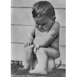 May include: Black and white photograph of a baby sitting on a chamber pot. The baby is looking down with their arms crossed over their knees. The chamber pot has a handle and is sitting on the ground.