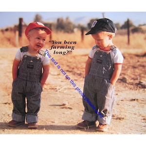 May include: Two young children wearing striped overalls, white t-shirts, and caps stand on a dirt road. One child wears a red cap, the other a black cap. The text "You been farming long?" is visible.
