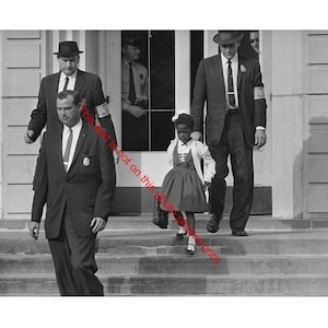 Puede incluir: Fotografía en blanco y negro de una niña con vestido y chaqueta, escoltada por hombres con trajes y sombreros. La niña lleva un bolso pequeño y baja unos escalones. Los hombres llevan insignias y brazaletes.