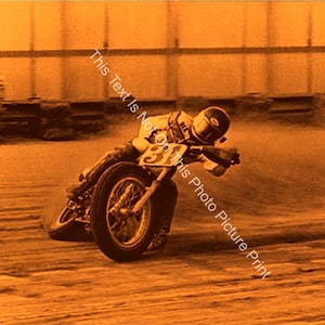 May include: A vintage photograph of a motorcycle racer in a helmet and racing suit, riding a motorcycle on a dirt track. The racer is wearing the number 31 on their racing suit. The photo is in sepia tones.