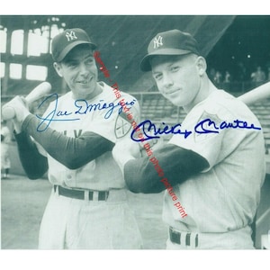 May include: Black and white photo of two baseball players in uniform, holding bats and signing autographs. The players are Joe DiMaggio and Mickey Mantle. The photo is signed by both players.