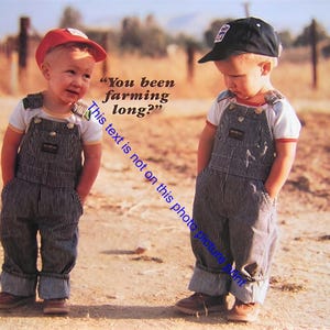 May include: Two young children wearing denim overalls and caps stand on a dirt path. One child wears a red cap, the other a black cap. Both have their hands in their pockets. The background shows a rural landscape.