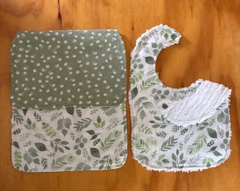 May include: A baby bib and burp cloth set. The bib has a white terry cloth collar and a leaf pattern. The burp cloth has a green polka dot pattern on top and a leaf pattern on the bottom. Both items are made of soft fabric.