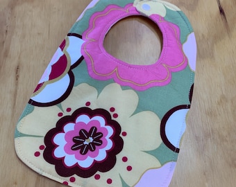 May include: A green, pink, and yellow floral baby bib with a white button.