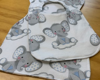 May include: White baby bibs with a repeating pattern of gray elephants sitting on clouds. The elephants have blue polka dot ears and are smiling. The bibs are made of soft fabric.