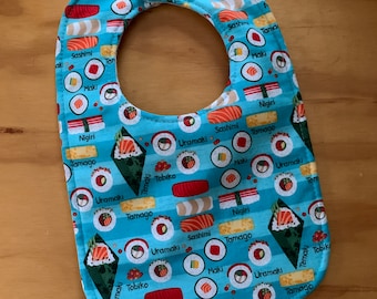 May include: A blue baby bib with a variety of sushi designs, including nigiri, maki, uramaki, tamago, sashimi, and tobiko. The bib is made of cotton and has a snap closure.