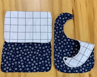 以下が含まれることがあります： 白い格子模様と紺色の花柄の布製のよだれかけ2枚。もう1枚は紺色の花柄と白い格子模様です。