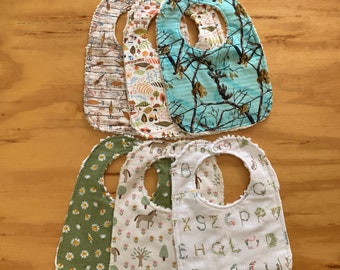 May include: Set of six baby bibs with different patterns. The bibs are made of soft, absorbent fabric and have a ruffled edge. The patterns include a woodland scene, a floral design, a geometric pattern, and a alphabet design.