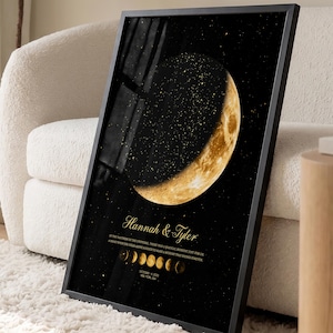 May include: A framed vertical wall art print featuring a large, golden crescent moon against a black, star-filled sky. Below the moon, the text reads Hannah & Tyler, followed by a sequence of moon phases and the date October 14, 2023.