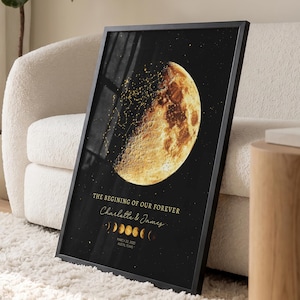 May include: A framed vertical wall art print featuring a large, detailed golden moon against a black background. The text reads THE BEGINNING OF OUR FOREVER, Charlotte & James, and includes a sequence of moon phases with a date and location below.