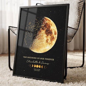 May include: A framed vertical poster featuring a large, detailed golden moon against a black starry background. The text reads THE BEGINING OF OUR FOREVER, Charlotte & James, and MARCH 22, 2022 AUSTIN, TEXAS, with a row of moon phases below the names.
