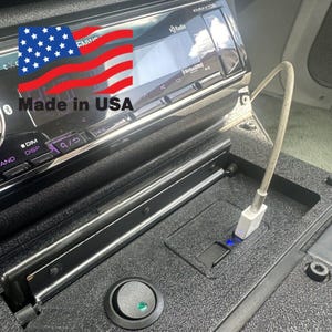 May include: A black car dashboard with a car stereo, a USB charging port, and a green toggle switch. The text "Made in USA" is visible on the stereo.