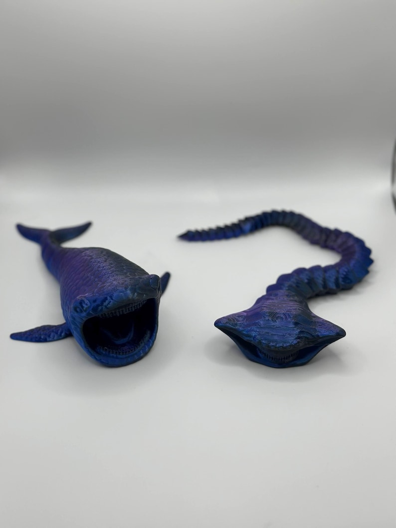 May include: Two 3D-printed, blue and purple sea creature models. One is a whale-like form with an open mouth, the other is a segmented, tentacle-like shape. Both are on a white background.