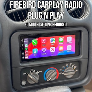 May include: A car dashboard with a new radio display showing app icons. The text "1993-2002 FIREBIRD CARPLAY RADIO PLUG N PLAY" is above the display, with "NO MODIFICATIONS REQUIRED!" below. The dashboard has air vents and climate control knobs.