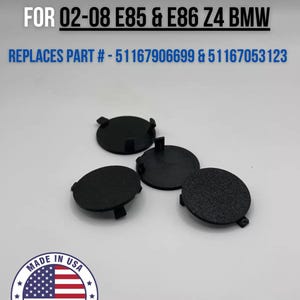 May include: Four black plastic screw caps for a center console. The caps are designed to replace parts # 51167906699 and 51167053123. The text "CENTER CONSOLE SCREW CAPS" and "FOR 02-08 E85 & E86 Z4 BMW" is printed in white on a black background. The text "REPLACES PART # - 51167906699 & 51167053123" is printed in black on a white background. The text "MADE IN USA" is printed in white on a red, white, and blue American flag. The text "FAST DELIVERY" is printed in white on a red background.