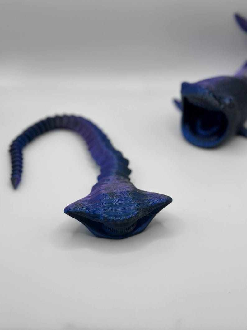 May include: Two 3D-printed, stylized whale shark models in shades of blue and purple. One model is complete with an open mouth, while the other is a detached tail section. The models have textured surfaces and are set against a white background.