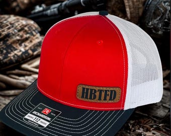May include: A red, white, and black trucker hat with the text "HBTFD" on a brown leather patch. The hat has a black brim with white stitching and a Richardson patch.