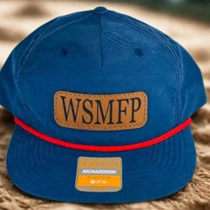 May include: A blue baseball cap with a brown leather patch displaying the letters "WSMFP". The cap has a red rope detail and a small tag with the brand name "Richardson".