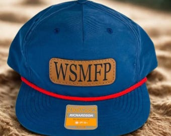 May include: A blue baseball cap with a brown leather patch displaying the letters "WSMFP". The cap has a red rope detail and a small tag with the brand name "Richardson".