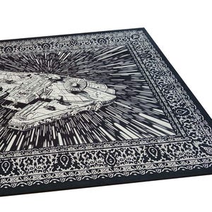 May include: Black and white Star Wars Millennium Falcon rug. The rug features a detailed illustration of the iconic spaceship against a backdrop of speed lines, with a decorative border. The rug is rectangular.